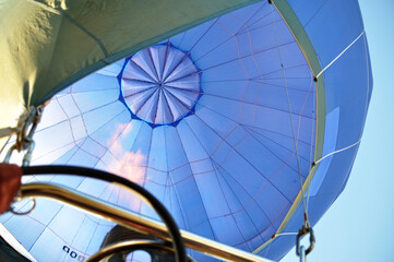View from a hot air balloon basket, looking up at the burner flame heating the blue envelope during flight