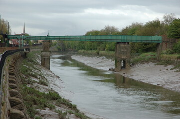 A green bridge spans a river with a church steeple in the background.