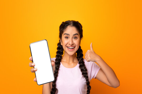 I Recommend. Portrait of excited young indian woman holding smartphone with black blank screen in hand, showing device and thumbs up sign gesture. Gadget with empty free space for mock up