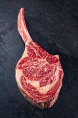Raw dry aged beef wagyu tomahawk steak offered as top view on black rustic background
