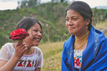 Indigenous girl showing red rose to smiling woman in andes mountains
