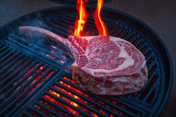 Barbecue dry aged angus tomahawk steak close-up on a charcoal grill with fire and smoke