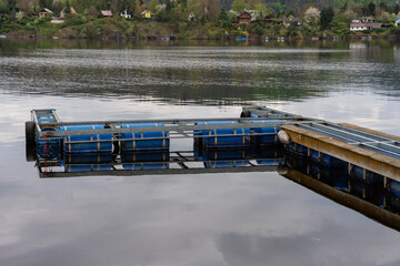 Floating dock made of metal frame and blue plastic barrels on still lake water. Industrial modular...