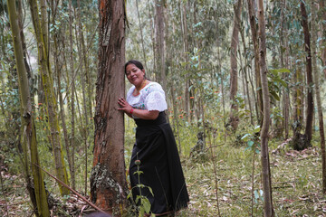 Indigenous woman wearing traditional clothes embracing a tree in a forest
