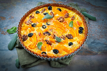 Homemade pumpkin savory tart quiche pastry with black olives, walnuts and fresh cheese served as close-up in baking form