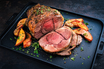 Traditional lamb leg roll roast with herbs and quince fruit served as close-up on a cast iron tray © HLPhoto
