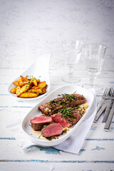 Juicy Easter lamb fillet roasted in butter with herbs and crunchy potato wedges served as close-up on a design plate © HLPhoto