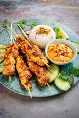 Sate ayam- grilled chicken satay sate skewers with peanut dipping spicy sauce, steamed rice and fresh cucumber served as close-up on a design plate