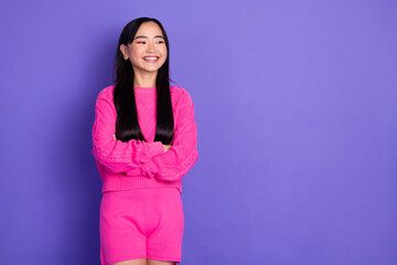 Cheerful young asian woman in stylish pink outfit posing against vibrant purple background in a...