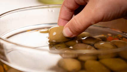 A close-up of a hand picking a green olive from a bowl. The image highlights healthy eating, snacks, and fresh food.