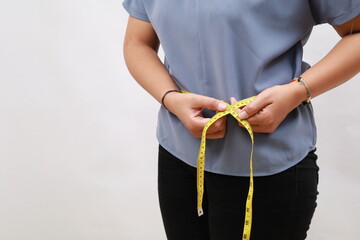Close up woman in blue shirt measuring her waist with yellow measuring tape. Weight loss, slim...