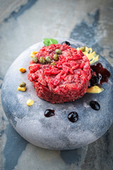 Gourmet beef tartar made of raw beef fillet with capers and  sauce drops served as close-up on a modern design plate