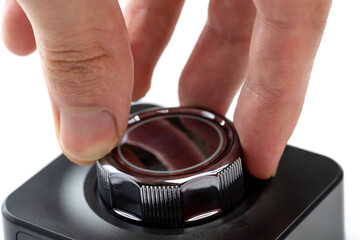 Fingers turning a shiny chrome control knob on a generic electronic device, rotating a dial for volume settings adjustment input, detail closeup, hand interaction textured dial ring simple concept