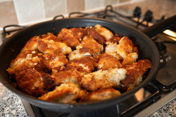 Close-up view of golden brown breaded chicken being fried in a black pan on a gas stove. The crispy coating and sizzling oil suggest the dish is almost ready to serve. High quality photo