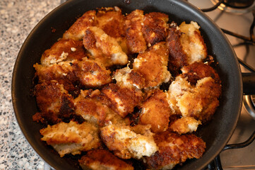 top view of breaded chicken pieces frying in a black pan on a gas stove. The food ready to eat with a golden, crispy crust. High quality photo