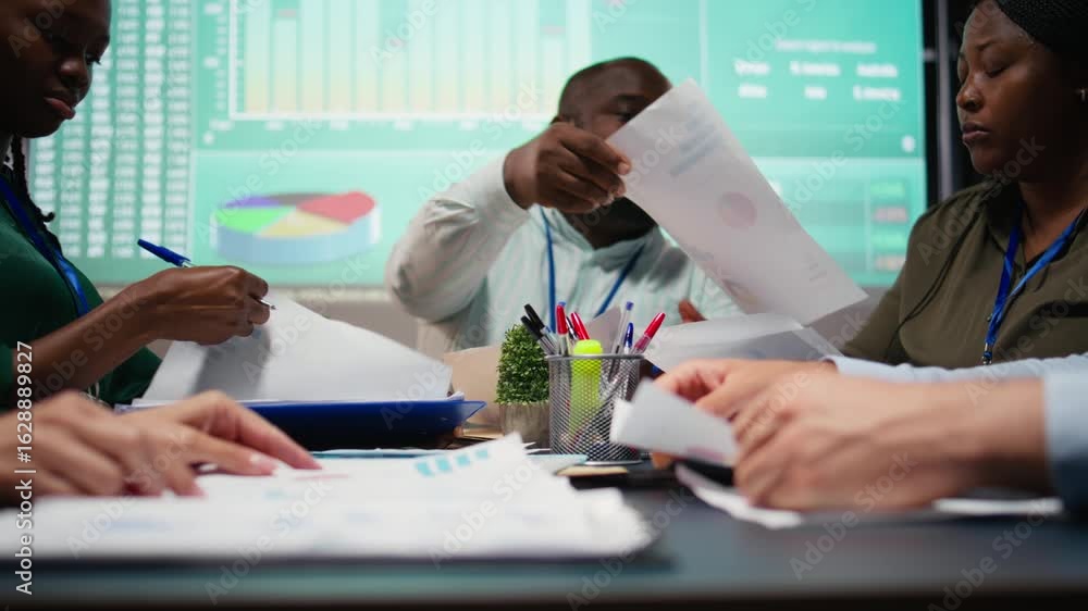 Poster Multiethnic team reviewing infographics to offer solutions to fix project issues, working after hours to finish tasks before deadline. Analysts attending problem solving meeting. Camera A.