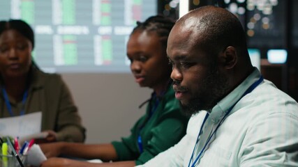 Black manager and his team studying annual data reporting during meeting late at night, looking into market supply and demands to facilitate global business development in boardroom. Camera B. - Powered by Adobe