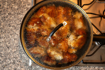 Overhead view of a frying pan covered with a glass lid, showing the chicken frying underneath....