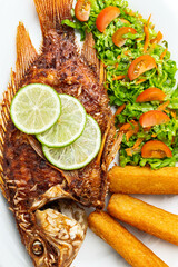 Traditional Colombian fried fish (Mojarra Frita), a whole tilapia served with fried yuca sticks and fresh salad, a typical main course from the Caribbean coast of Colombia, on a white background