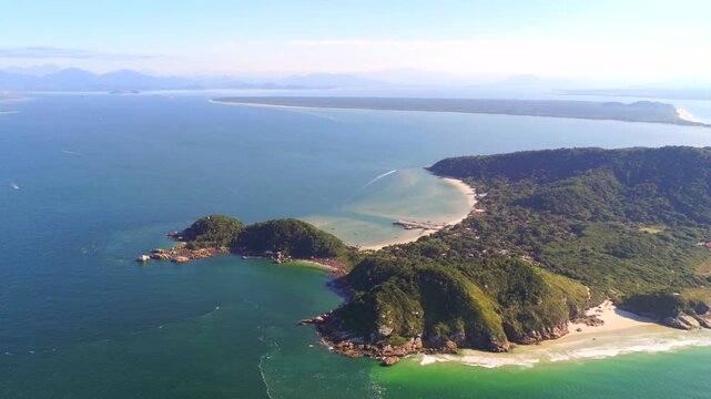 Drone view of Ilha do Mel coastline with beaches, forested hills and boats in the sea.