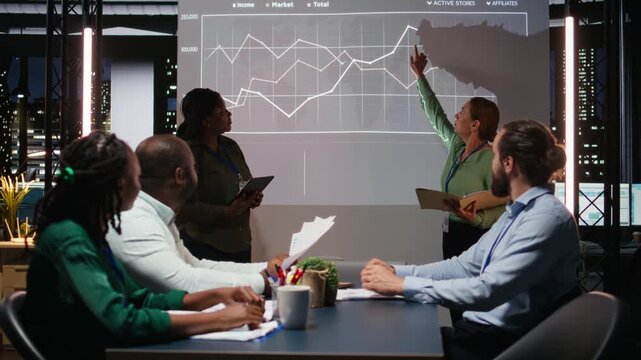 Multiethnic experts team evaluating data performance metrics on projection board, reviewing data insights with investors group in executive session after hours. Corporate event at night. Camera A.