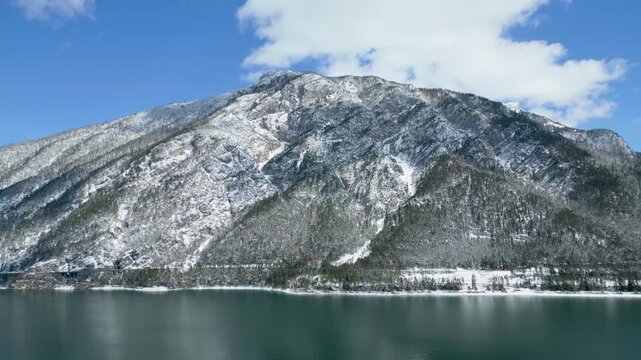 Panoramic drone shot of a breathtaking snow-covered mountain rising majestically from the tranquil turquoise lake in the heart of the Alps