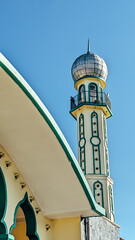 Low angle view. A particular minaret of the mosque featuring a balcony near the top and a domed roof with a clear blue sky as background