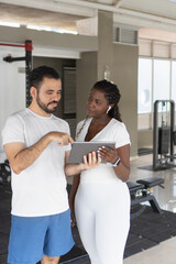 Personal trainer showing workout routine on tablet to client in gym