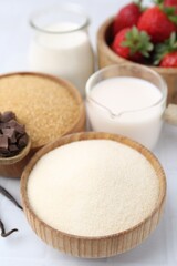 Different ingredients for panna cotta. Milk, sugar, vanilla, chocolate and strawberries on white tiled table, closeup