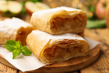 Pieces of tasty apple strudel with powdered sugar and mint on wooden table, closeup