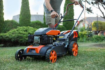 Man pulling starter cord of lawn mower in garden, closeup