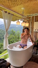 Handsome Man Soaking in Bubble Bath with Breathtaking Mountain Sunset View in his honeymoon trip