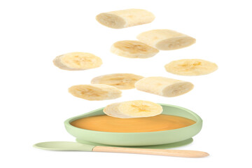 Baby food. Banana slices falling into bowl of puree on white background
