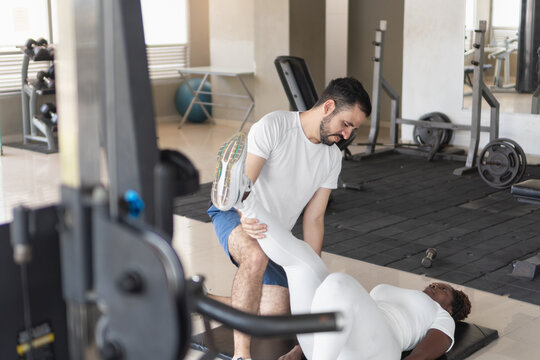 Personal trainer helping client stretching legs in gym