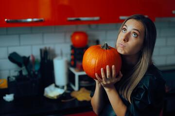 Puzzled Housewife Holding a Pumpkin in her Kitchen. Pensive party host trying to prepare something...