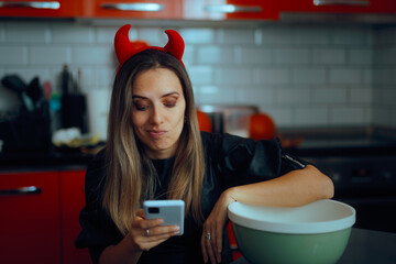 Woman Wearing Devil Costume Checking her Phone. Puzzled party host checking recipe in cooking app