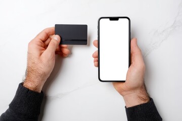Hands holding a black credit card and a smartphone with blank screen on a white marble surface