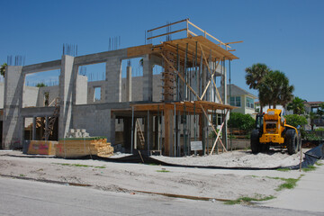 Residential two story Building Under Construction With Materials and Tools Onsite. Under a clear sky, a new house structure undergoes construction, showcasing tall walls, open frames, and stacked buil