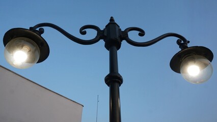 Twin vintage street lamps in silhouette against a fading dusk sky, with soft city structures barely...