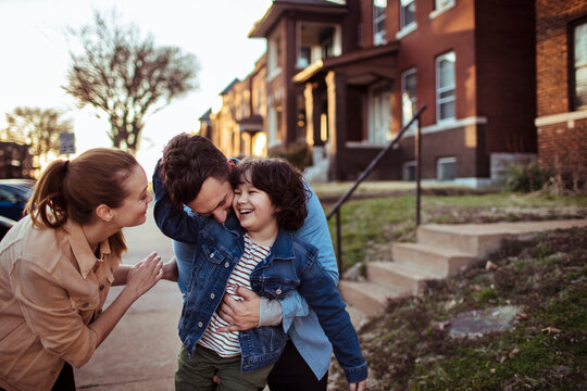 Happy parents playing and laughing with their child outside suburban home at sunset