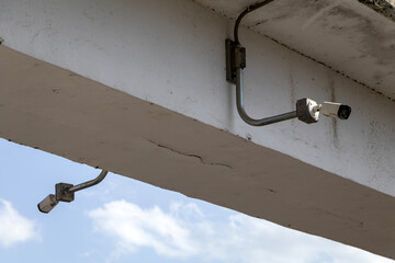 CCTV security camera mounted under a pedestrian bridge, monitoring both directions of a city street for safety and surveillance purposes.