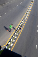 Aerial perspective from a pedestrian bridge showing a person jaywalking across a street without using a crosswalk, highlighting urban life and traffic behavior.