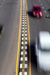 High-angle shot of a black and white road median separating two lanes of fast-moving traffic, illustrating urban speed and infrastructure.