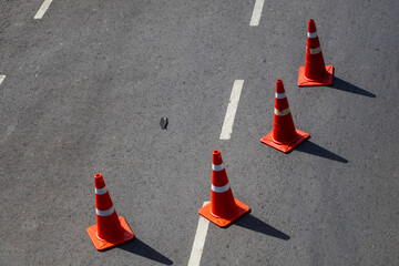Four orange traffic cones placed on asphalt road with a discarded black face mask nearby, symbolizing urban safety and pandemic aftermath.