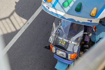 Top-down view of a traditional Thai tuk tuk parked in the shade, patiently waiting to pick up passengers under the bright sun.