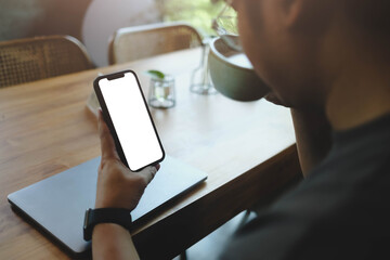 A person relaxing in a cafe, looking at a smartphone with a blank white screen while drinking coffee. A perfect mockup for lifestyle apps.