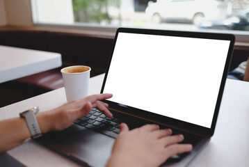 A person's hands typing on a laptop with a blank white screen by a window, ideal for showcasing websites or business content in a modern workspace.