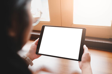 A person holding a tablet computer horizontally with a blank white screen by a sunlit window, perfect for displaying video or landscape content.