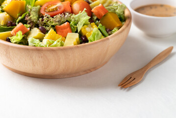 Healthy vegetable salad in wooden bowl with Japanese sesame dressing and fork on white background