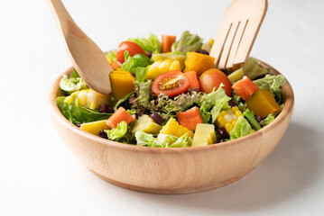 Healthy vegetable salad mixing in wooden bowl on white background